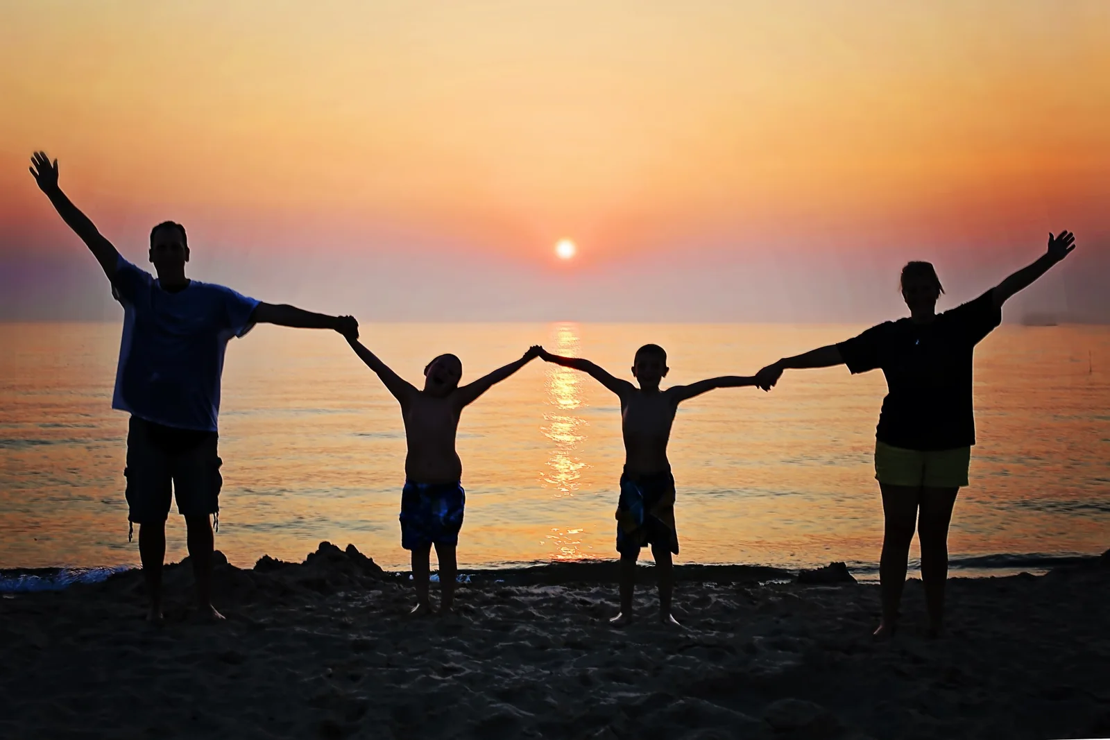 Family holding hands with arms raised at sunset