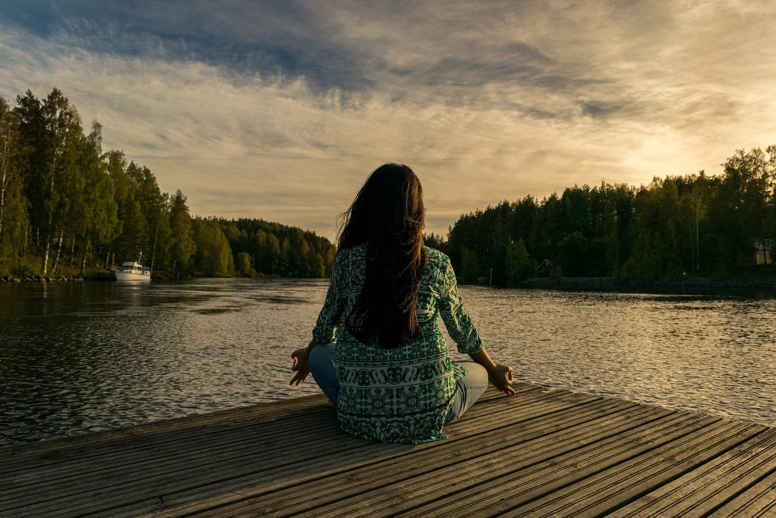 Person seated on a wooden dock beside a lake